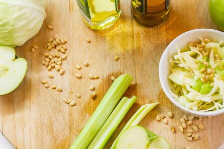 Salad with fresh cabbage, celery, apples and pine nuts, drizzled with olive oil in a salad bowl on a cutting board among the vegetables and herbsの写真素材