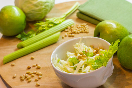 Salad with fresh cabbage, celery, apples and pine nuts, drizzled with olive oil in a salad bowl on a cutting board among the vegetables and herbsの写真素材