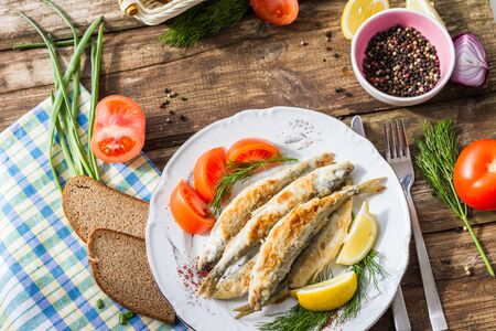 Fried fish smelt on a plate, served with lemon, tomatoes, onions and herbs.の写真素材
