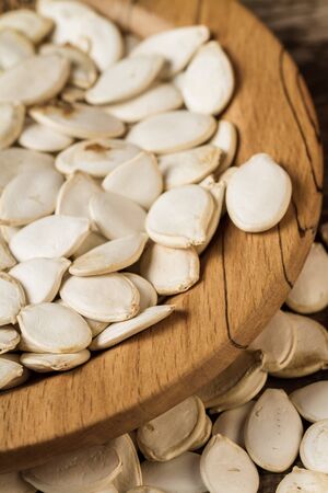 Organic white pumpkin seeds on a wooden plate.の写真素材