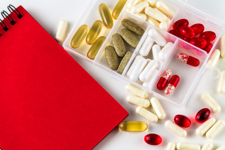Various medical color capsules, pills and notebook for records on a white background.の写真素材