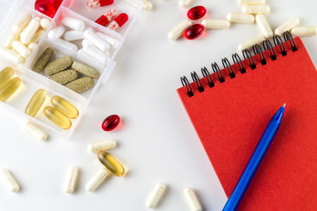 Various medical color capsules, pills and notebook for records on a white background.の写真素材