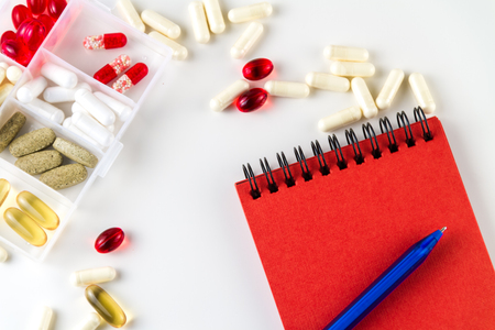 Various medical color capsules, pills and notebook for records on a white background.の写真素材