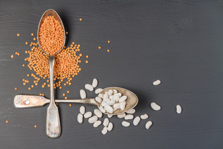 Natural red lentil and white beans in silver spoons on a black background.の写真素材