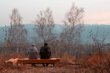 man and woman sitting on a bench in the park in the fallの写真素材