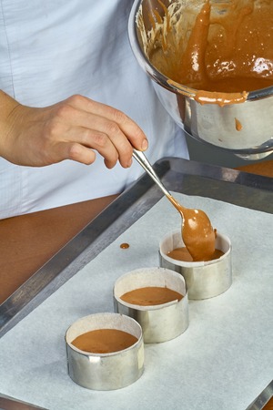 The cook pours the dough into forms for making cupcakesの写真素材