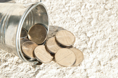 Silver bucket with coins. Coins in and near the bucket. The bucket is on its side. Business,...