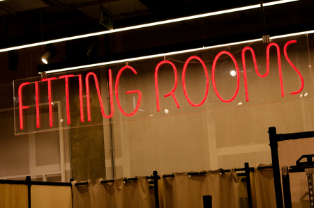 Glowing red text FITTING ROOMS in a modern  clothing store. Neon text on the signboard. The inscription inviting visitors to try on your favorite clothes before buyの写真素材