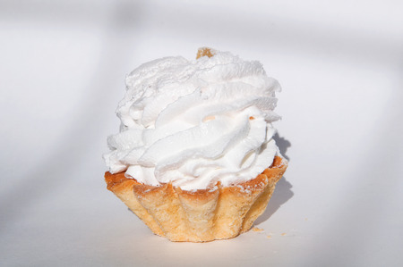 Beautiful cake with protein cream on white background with a shadow in the form of a coarse grid. Airy protein cake basket from whipped egg white with sugar.  Slice of marmalade on the top of cake.の写真素材
