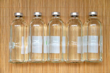 New medical bottles for infusions with physiologic saline on wood bamboo place mat texture background. Group of five bottles on the same level. Bottles  for saline IV drip dropper. View from above.の写真素材