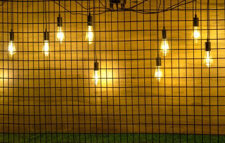 Glow lamps in different positions on wires behind metal grid. Decorations if cafe or pub.の写真素材
