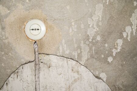 Old electrical outlet without grounding on the old gray wall. Round plastic wall socket on the plastered with cement wall.  Copyspace for text. The concept of repairing old apartments.の写真素材