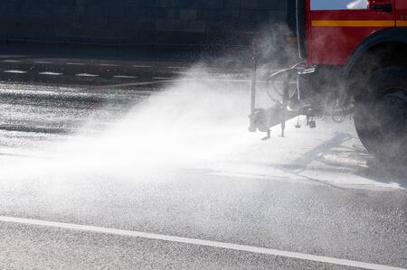 Watering machine washes the road dust, dirt and viruses in a city. Water mist and spraying water particles at sunny day near the asphalt. Cropped view of road cleaning.の写真素材