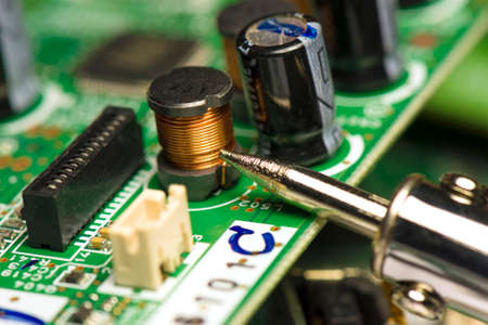 Electronic components soldered in circuit board. A soldering iron plated on a green printed circuit board. Copper Wire Ferrite Choke. Close-up of a soldering iron tip.の写真素材