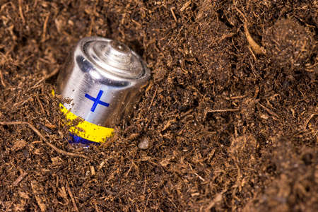 Ðart of the AA battery sticks out of the ground. Used battery in the soil. Recycling of batteries. Concept of soil pollution and environmental protection from heavy metals and toxic elements.の写真素材