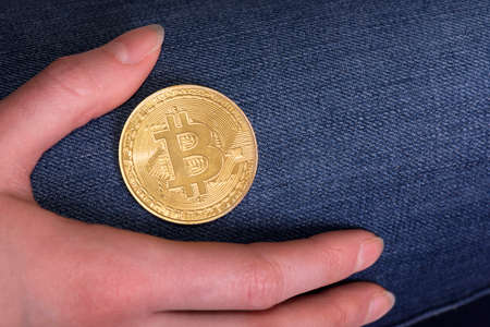 Bitcoin and woman's hand lie on leg with jeans. Free space for text.の写真素材