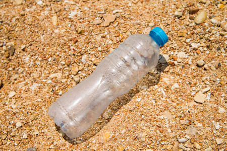 Transparent empty plastic drink bottle with blue cap on the sand. There are drops of water on the walls of the bottle. Ð¡oncept of global pollution of the planet with plastic.の写真素材