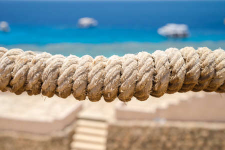 Close-up of horizontal marine rope in the center of the picture with bokeh background. Sunny day. Blurred background of blue water of the Red Sea with boats and stairs to the sea.の写真素材