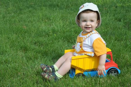 a smiling baby with a pacifier is sitting in the toy truck on the grassの写真素材