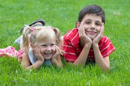 a little girl and a boy are lying on the grass in the park の写真素材