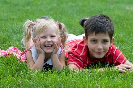 a little girl and a boy are lying on the grass in the parkの写真素材