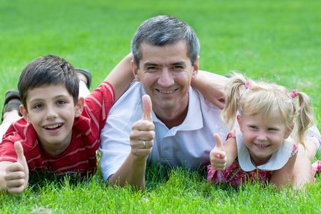 a man, a little girl and a boy are lying on the grass in the parkの写真素材