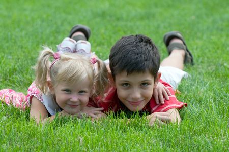a little girl and a boy are lying on the grass in the parkの写真素材