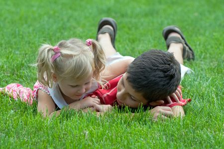 a boy and a little girl are lying on the grass in the parkの写真素材