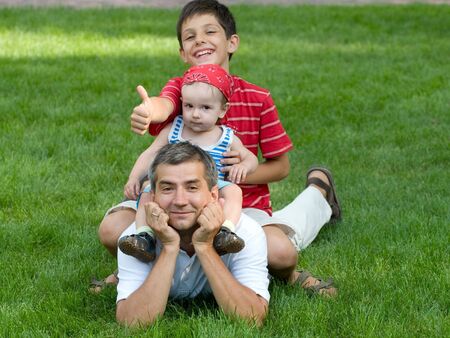 two sons are sitting on their father's back holding thumbs upの写真素材