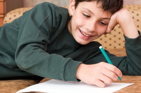 a smiling boy writes a letter on the sofaの写真素材