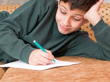 a smiling boy writes a letter on the sofaの写真素材