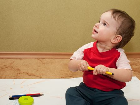 An inspired toddler is sitting on the floor and thinking about his drawingの写真素材