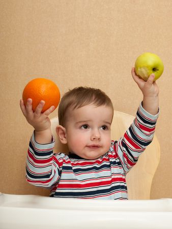 A baby is holding an apple and an orange in his handsの写真素材