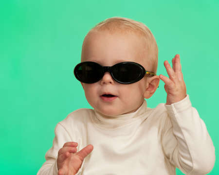 An important toddler in glasses is sitting on the green backgroundの写真素材