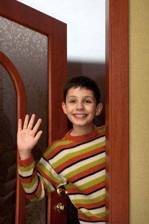 A happy boy is leaving a room and waving farewellの写真素材
