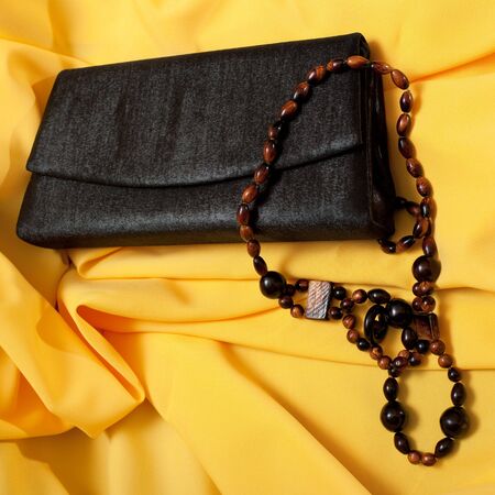 Black purse and wooden neclaces on yellow backgroundの写真素材