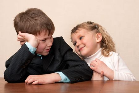 A boy in suit and a girl in white are talking at the class desk の写真素材