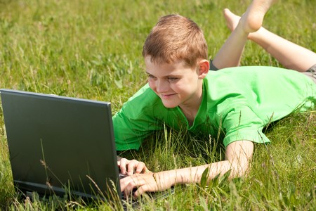 A happy boy with a laptop is smiling on the grassの写真素材