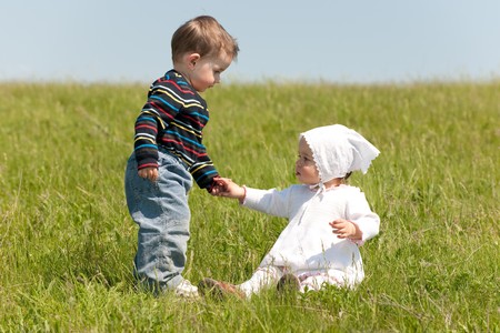 A toddler boy helps a toddler girl to get up in the meadow  の写真素材