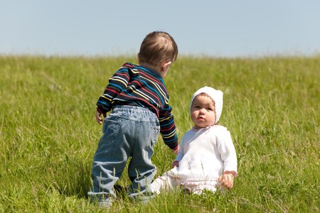 A little boy helps a toddler girl to get up in the meadowの写真素材