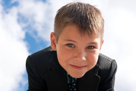 A smiling boy in suit is standing outdoors against the skyの写真素材