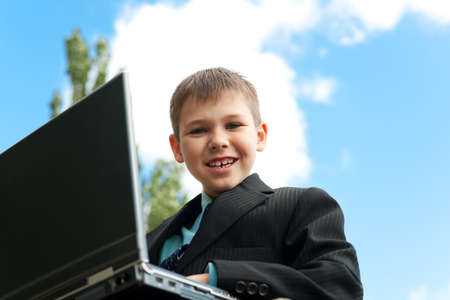 A smiling boy with a laptop is studying outsideの写真素材