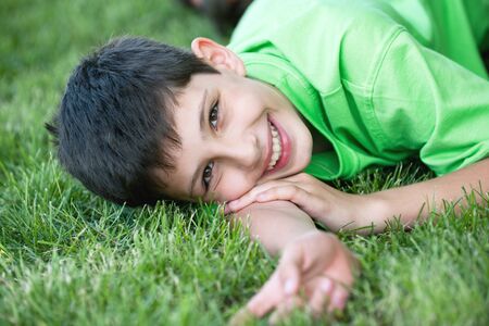 Happy smiling boy in green is lying on the summer meadowの写真素材