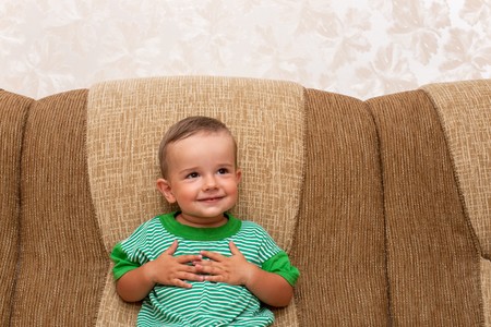 A smiling little boy is sitting on the sofaの写真素材
