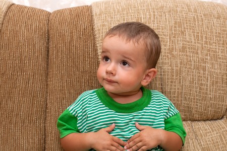 A serious little boy is sitting on the sofaの写真素材