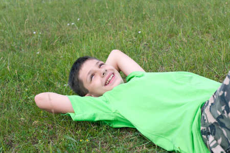 A smiling boy is lying on the green summer meadowの写真素材