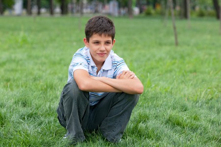 A thoughtful  boy is sitting on the grassの写真素材