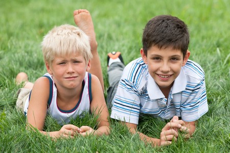 Thoughtful and smiling boys are lying on the green grass の写真素材