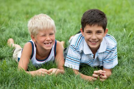 Two friendly handsome boys are lying on the green grass の写真素材