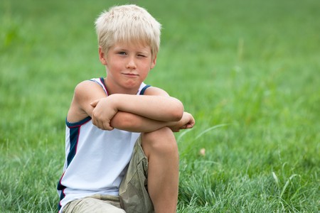 A thoughtful  boy is sitting on the green grassの写真素材